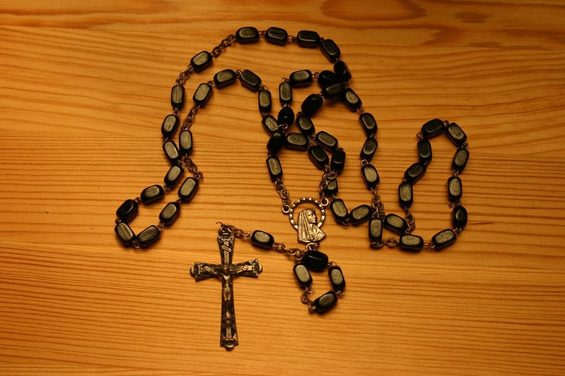 Judge's ruling spotlights legal challenges in clergy abuse settlements A dark brown rosary on a medium brown wooden table.