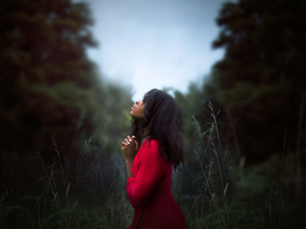 Church of England’s new anti-racist toolkit sparks debate A woman in red stands outside with hands clasped by chin and head lifted to the sky.