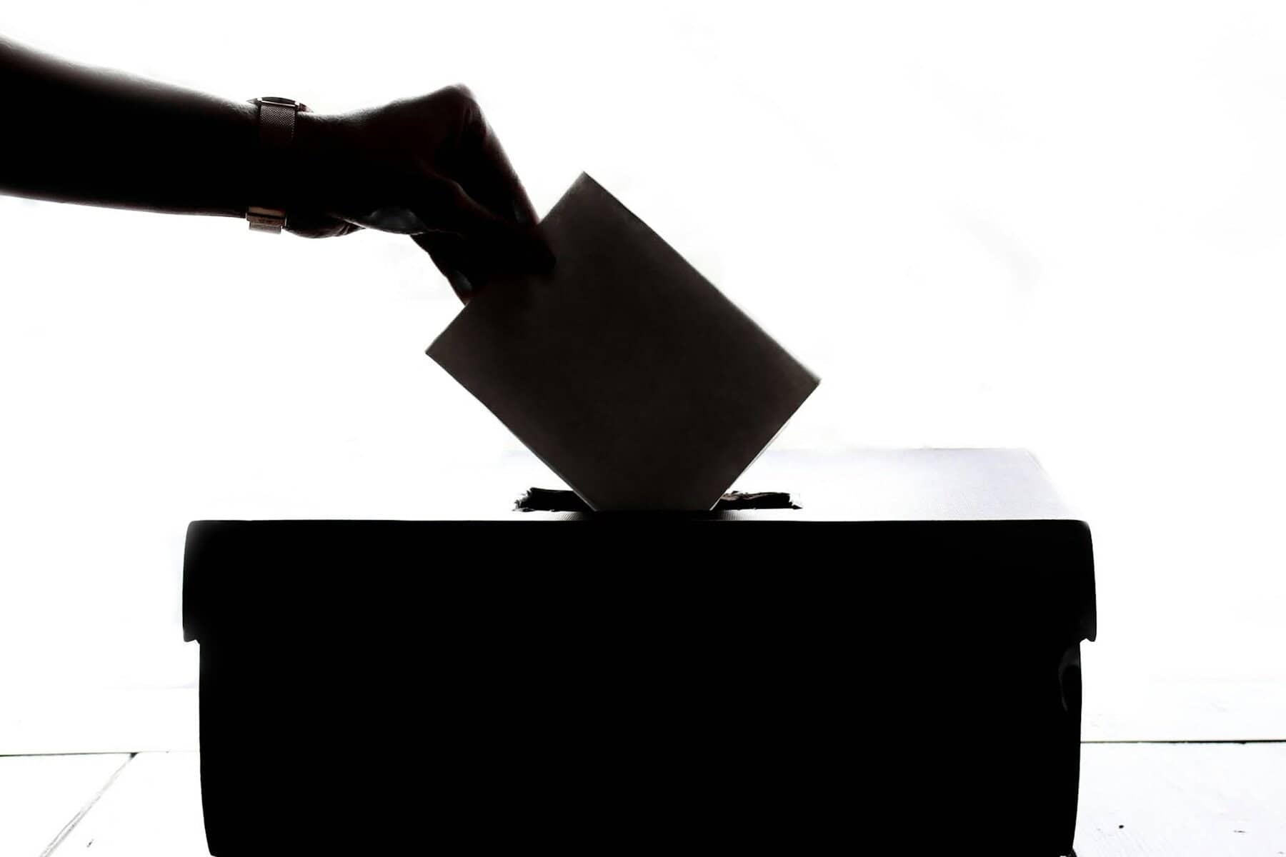 A hand dropping a ballot into a box.