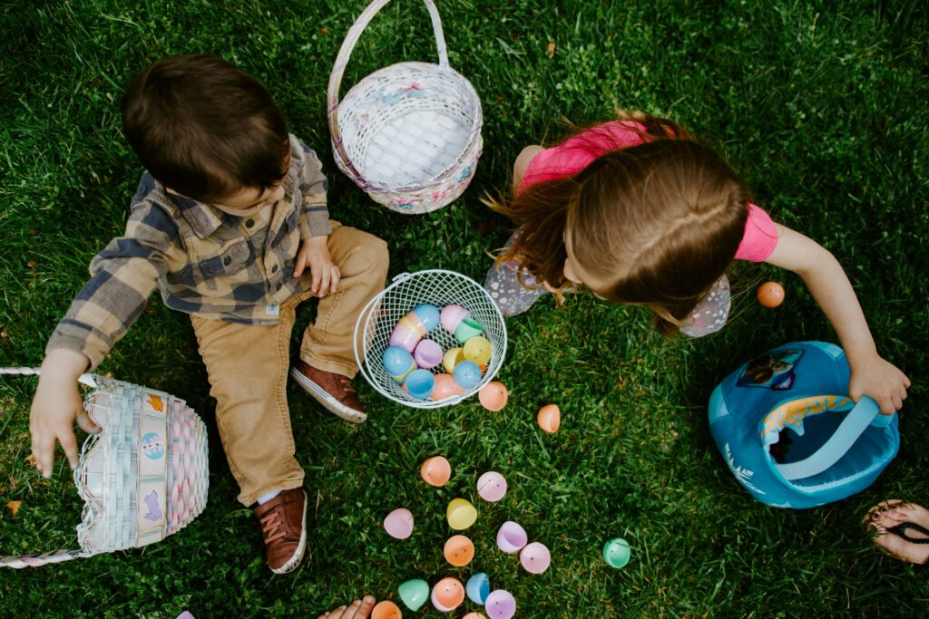 Seen from directly overhead, two children sit on grass with easter baskets.