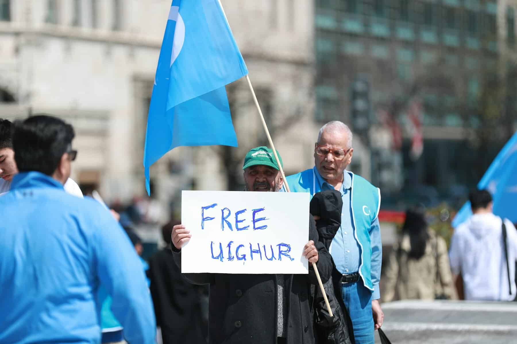 A man stands with a protest sign supporting Uighur.
