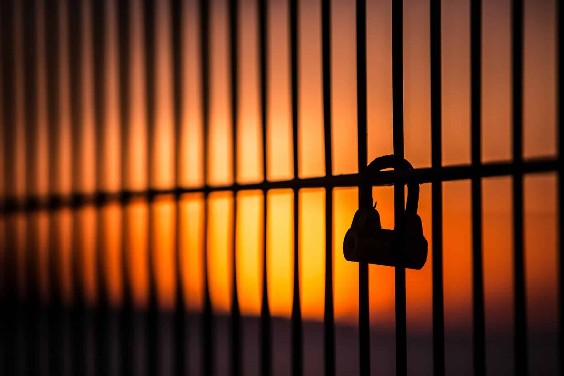Lock on a metal fence with orange sunrise behind.