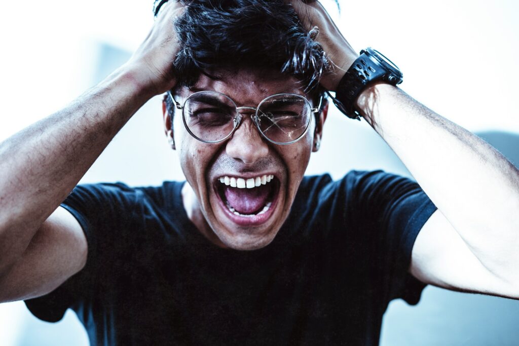 A man has hands in his hair, is yelling with a broken glasses lens.