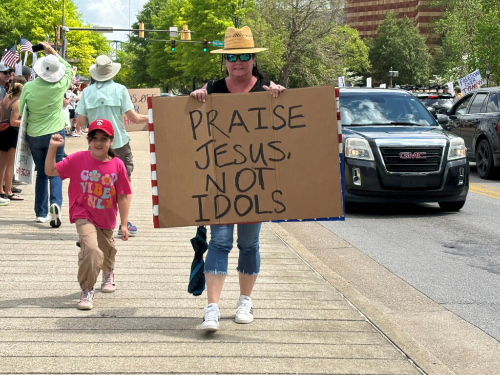 Why United Methodists are speaking out against service cuts Protestor with sign, Praise Jesus not idols