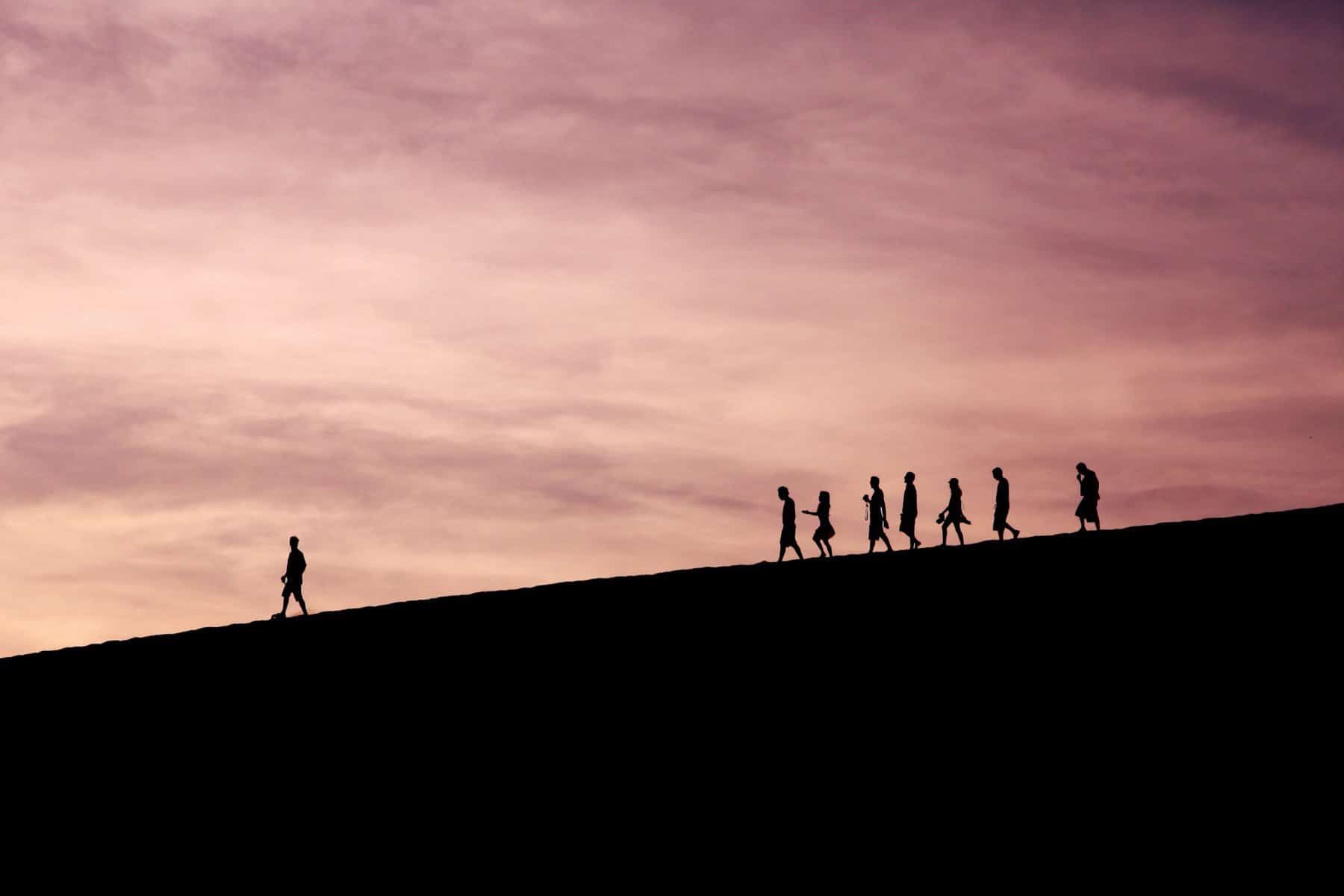 Silhouettes of people in a line with one leading from a bit ahead.
