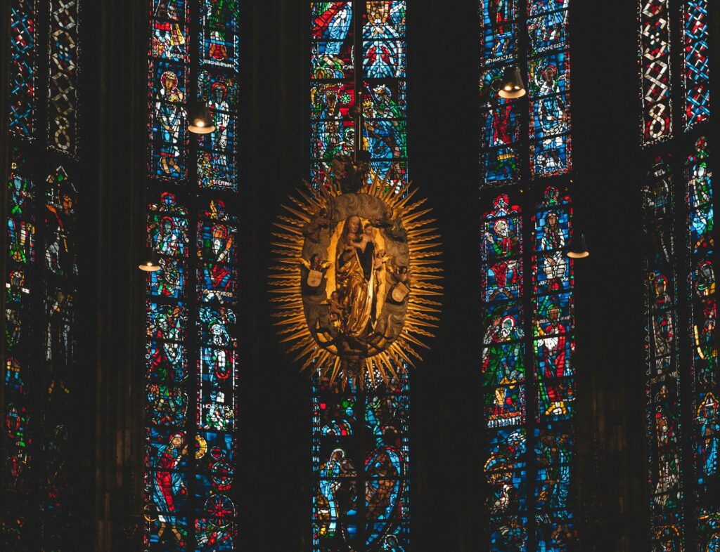 A Madonna and child piece of art in front of stained glass.