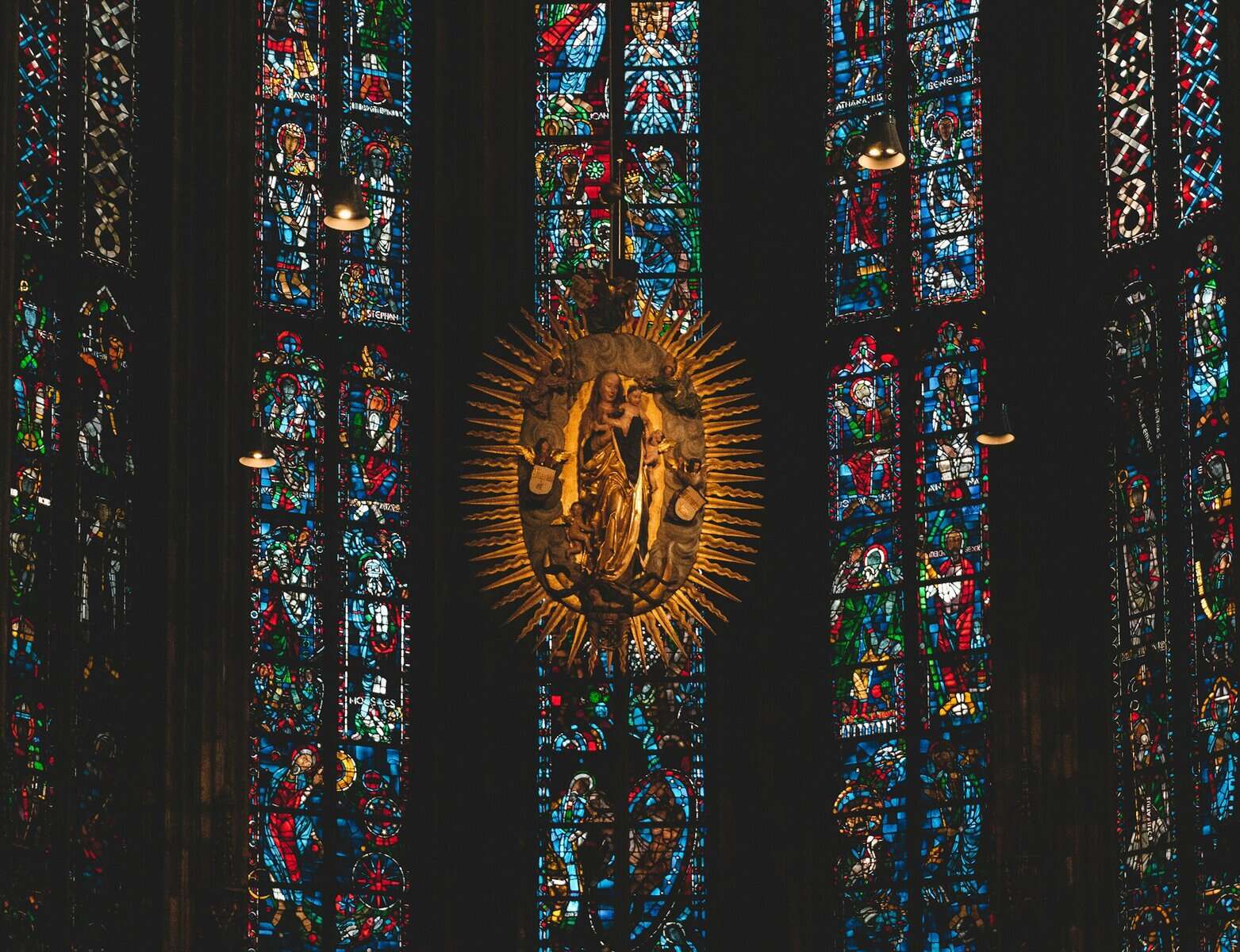 A Madonna and child piece of art in front of stained glass.