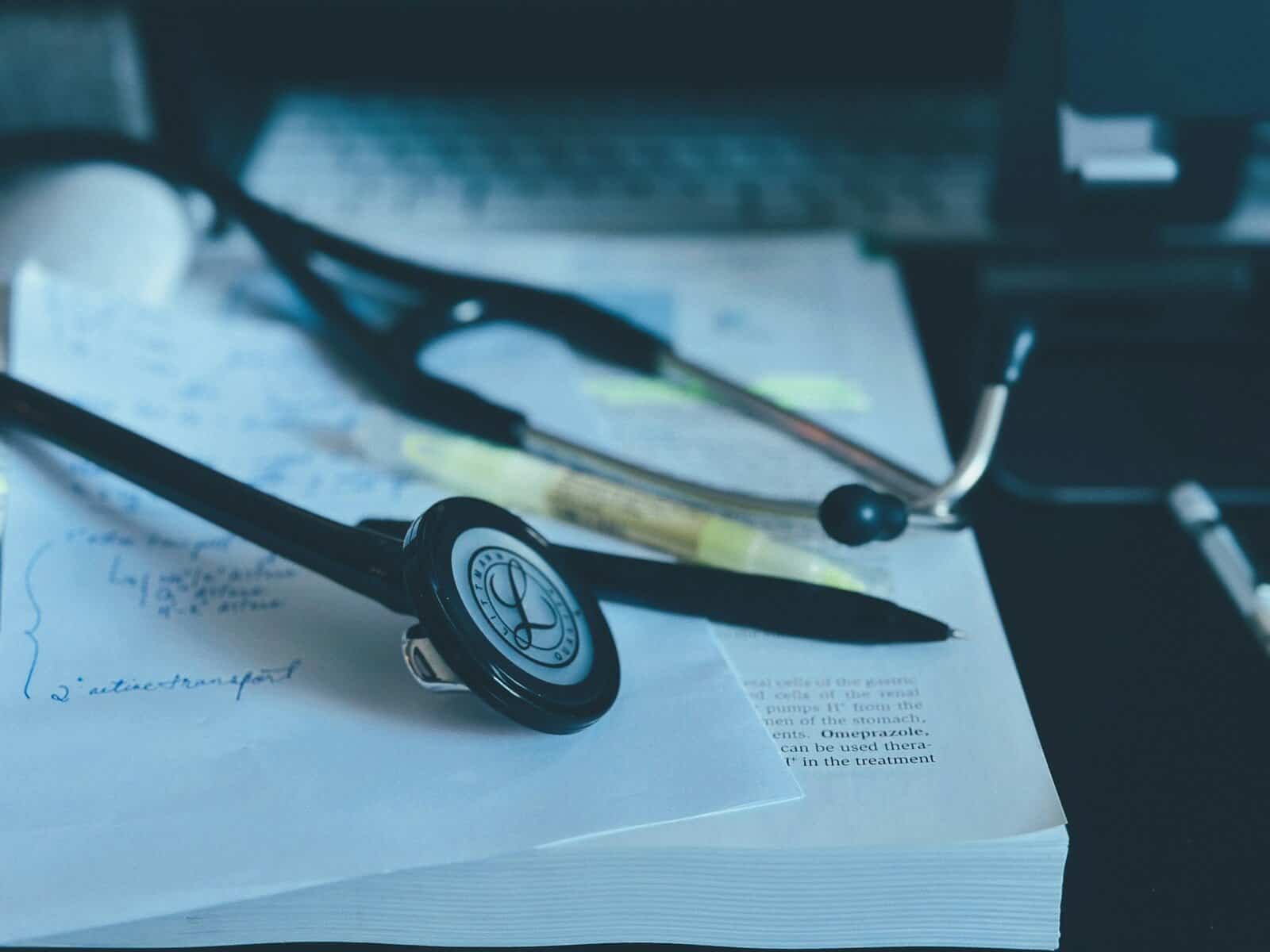 A stethoscope sits on a book with notes and a pen.