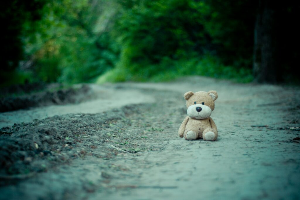 A teddy bear sits alone on a gravel road.