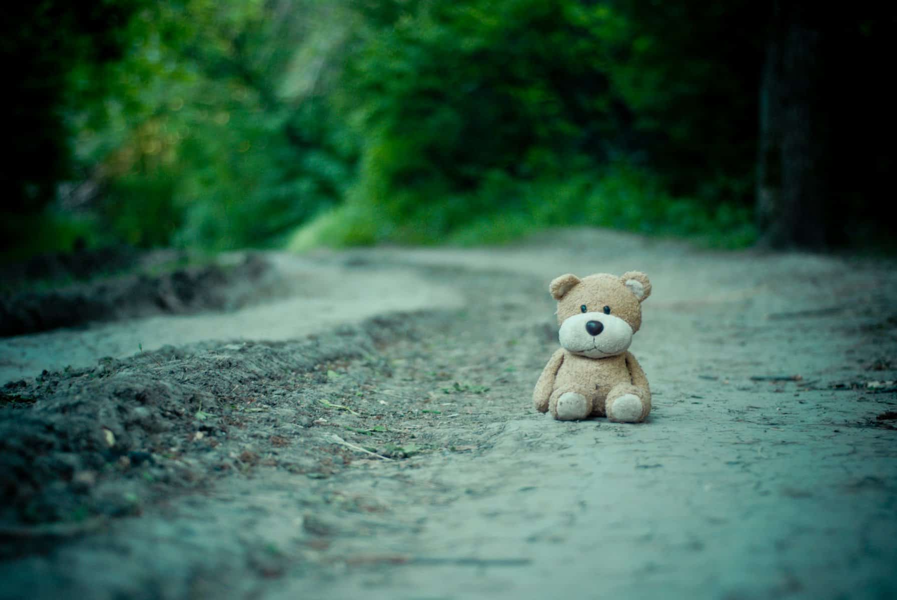A teddy bear sits alone on a gravel road.