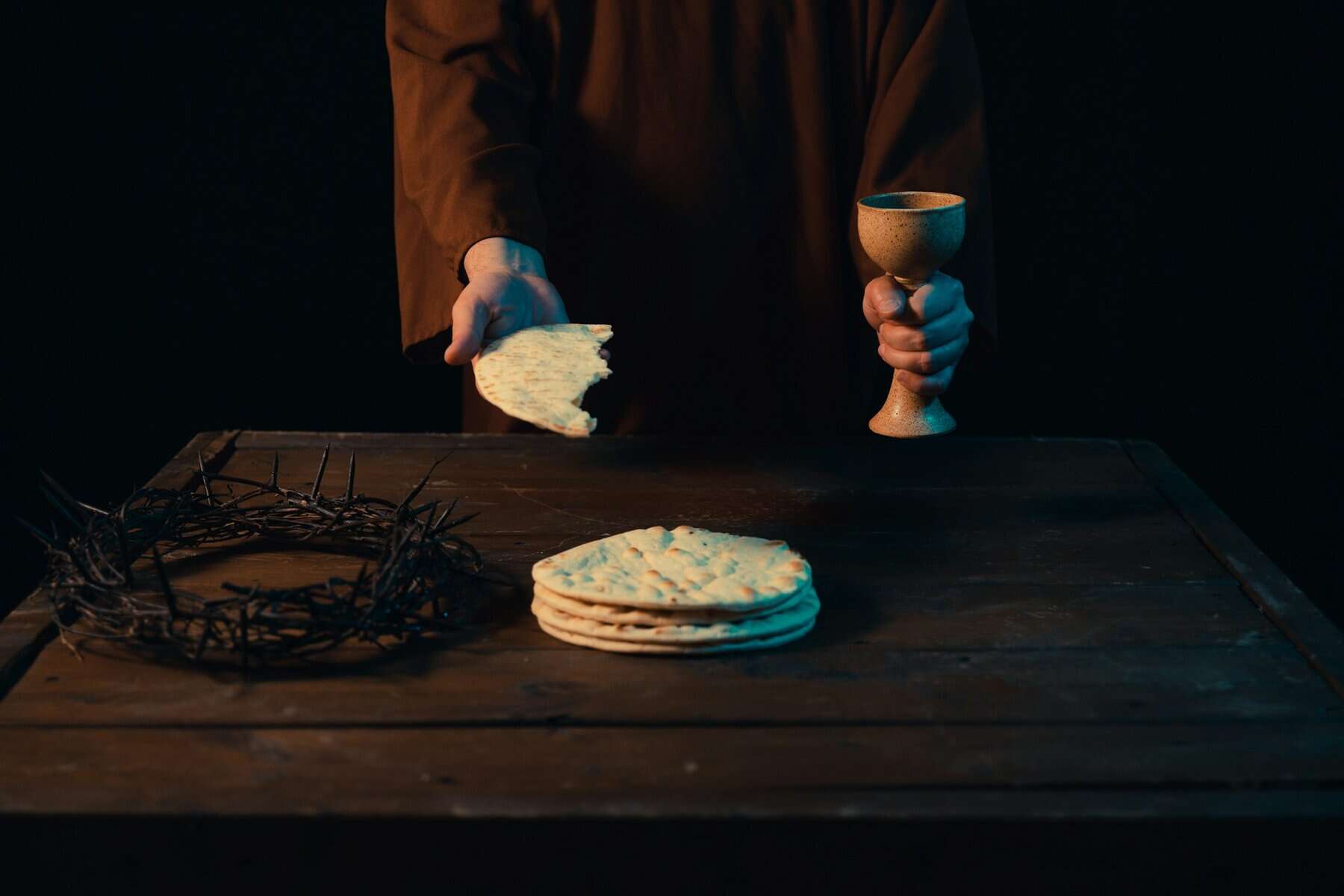 A person holding bread and a wine goblet with a crown of thorns next to them.