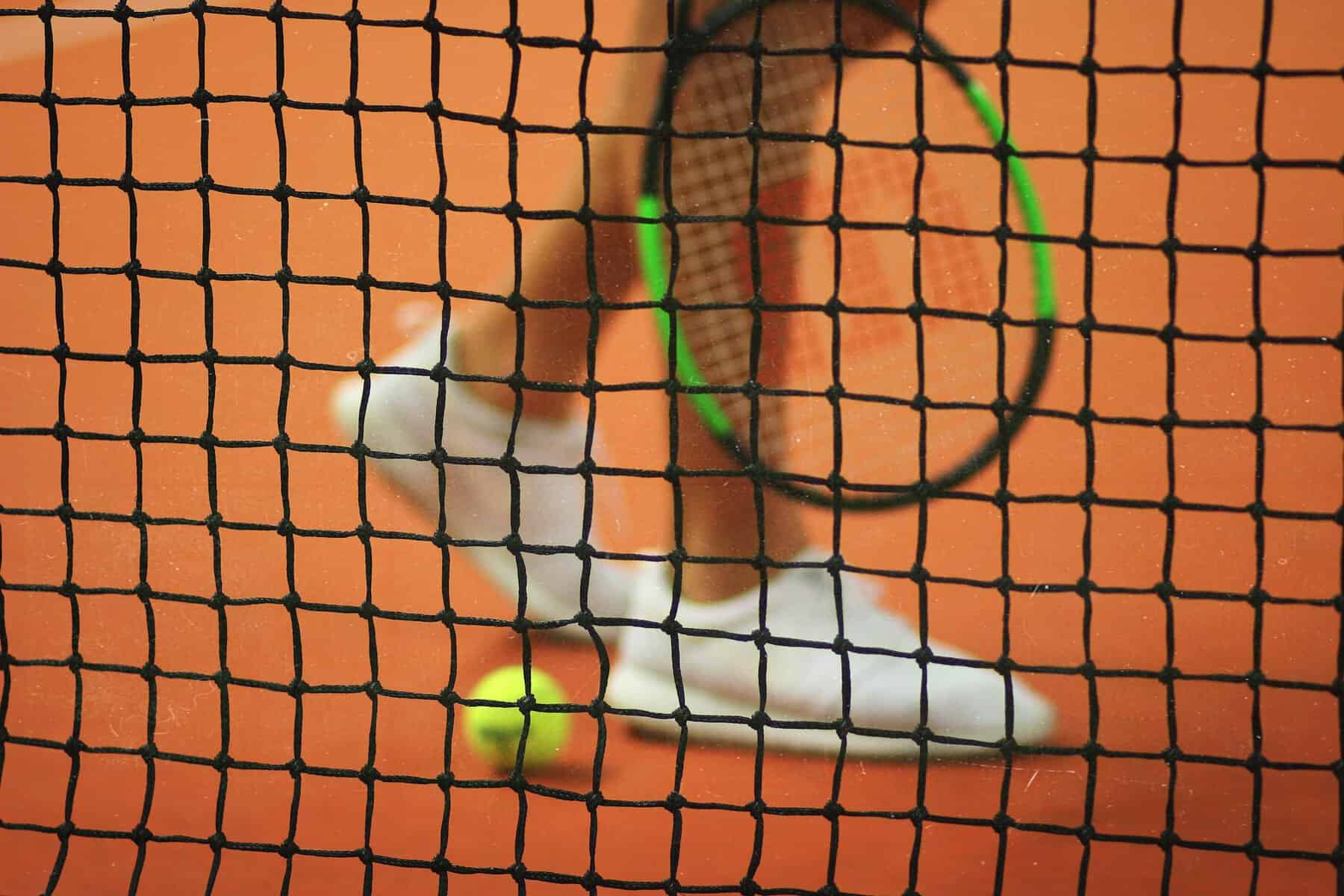 Tennis net with a player, racquet and ball in the background.
