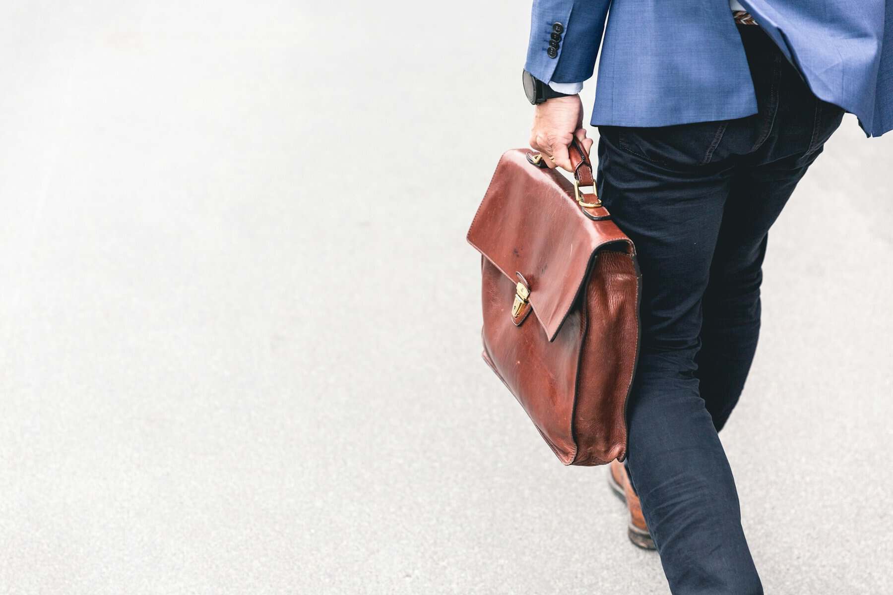 Man holding leather satchel walking away from camera.