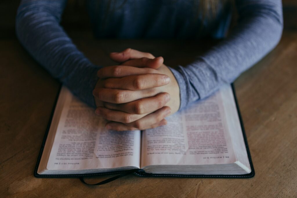 How education impacts religious attendance in the U.S. and Europe A man's hands are shown clasped and resting on a a Bible.