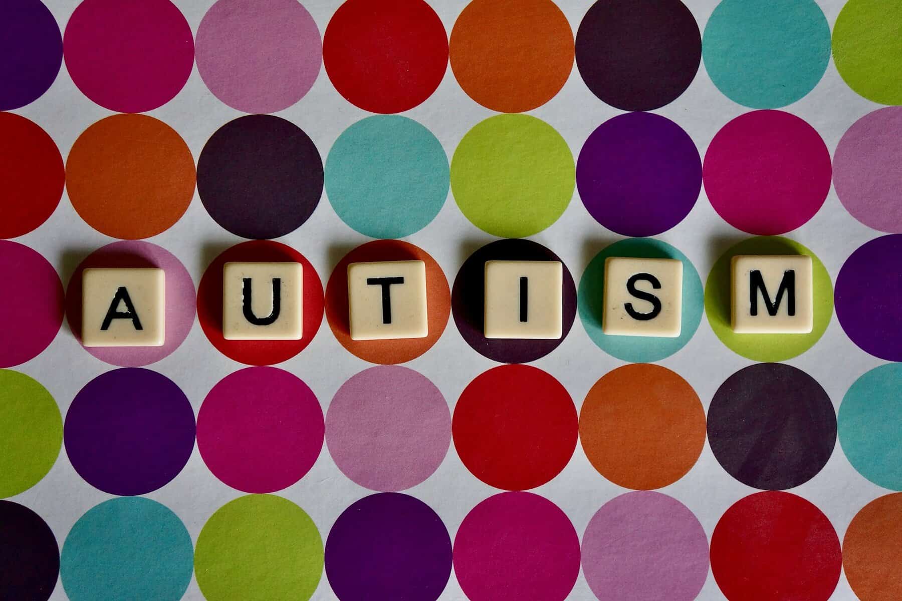 "Autism" spelled on Scrabble tiles on a polka-dotted background.