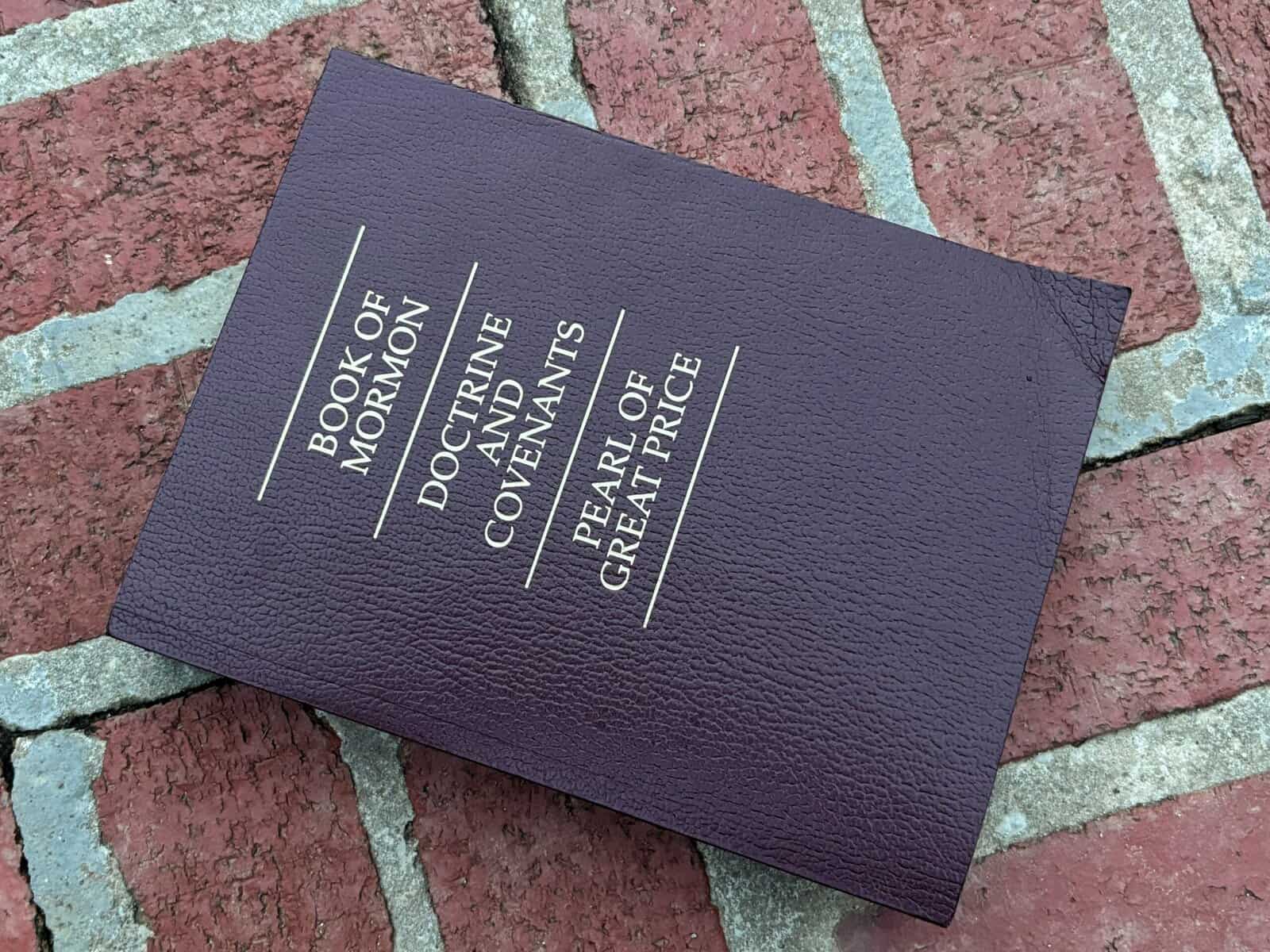 A Book of Mormon on a brick patio.