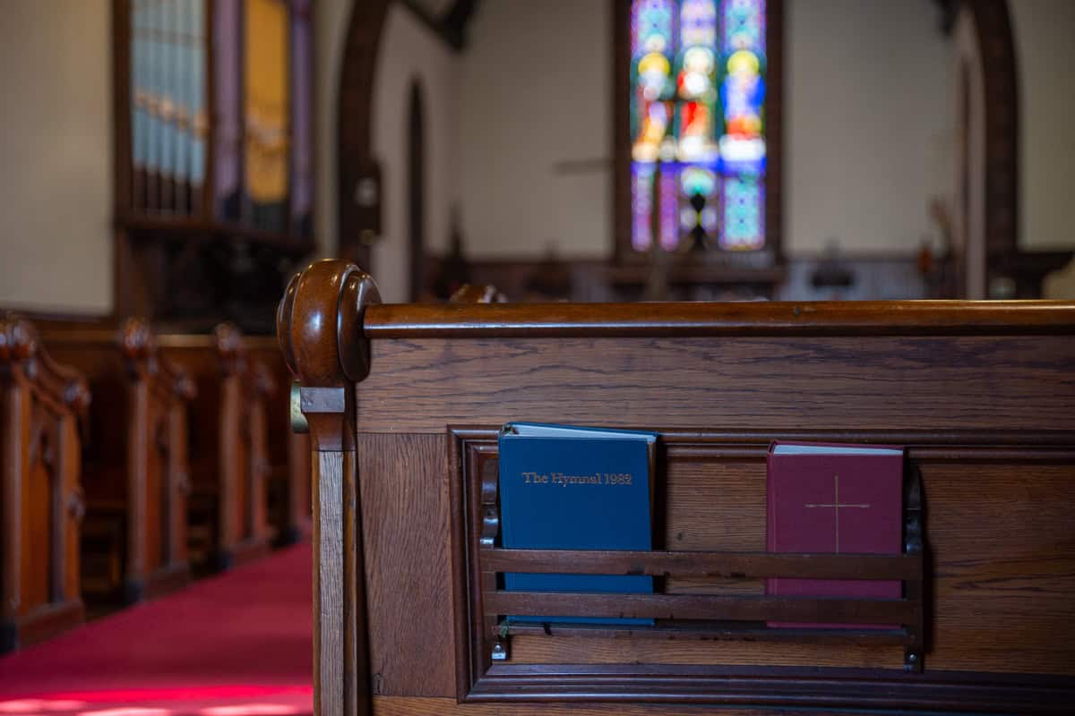 Inside of a small church/chapel with a pews and hymnals in the back of the pew.