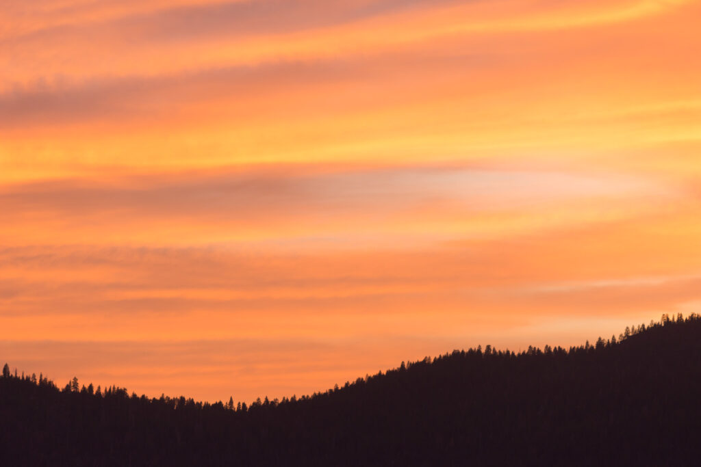 Theologian Walter Brueggemann remembered for his prophetic voice Vibrant orange sunset with a mountain ridge with pine trees.