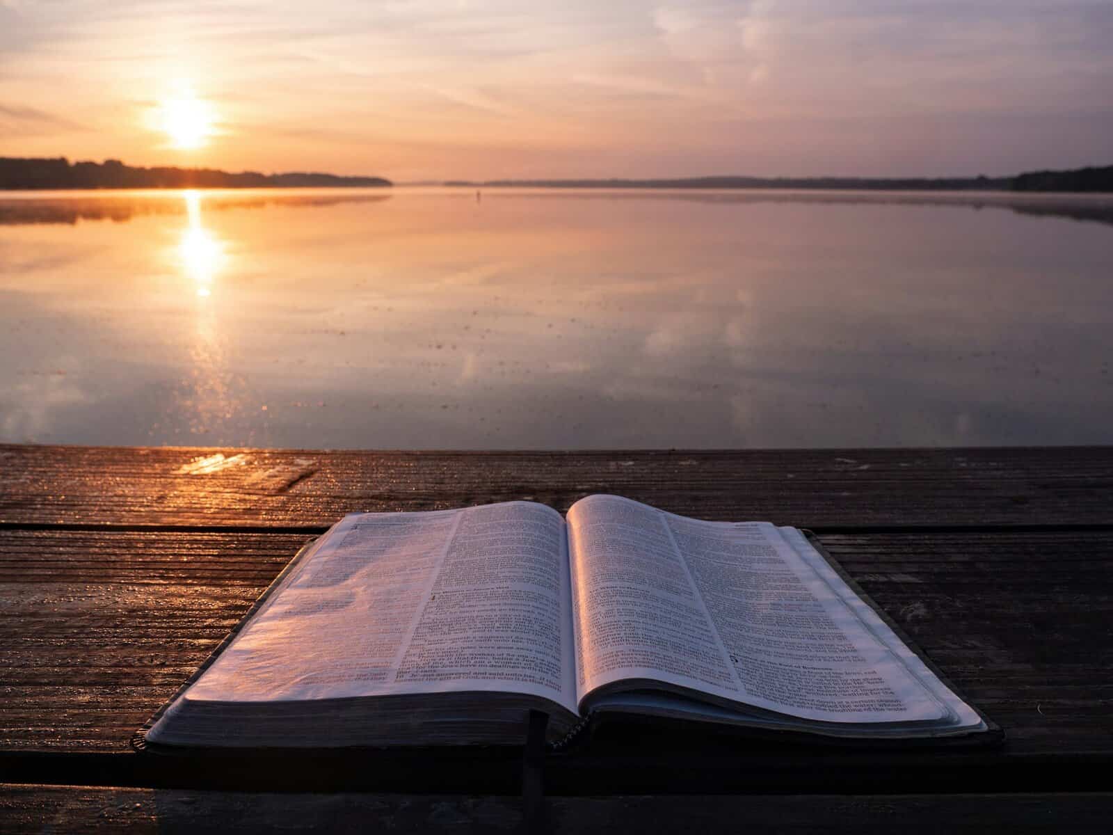 An open Bible sitting on a dock at sunset.