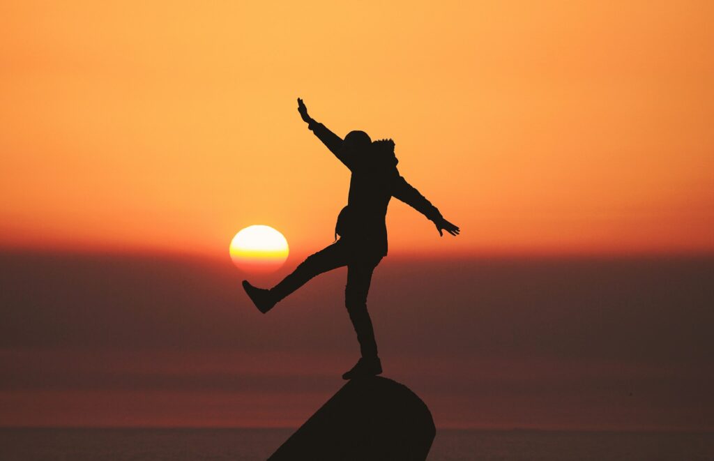 A person balancing on a rock at sunset.