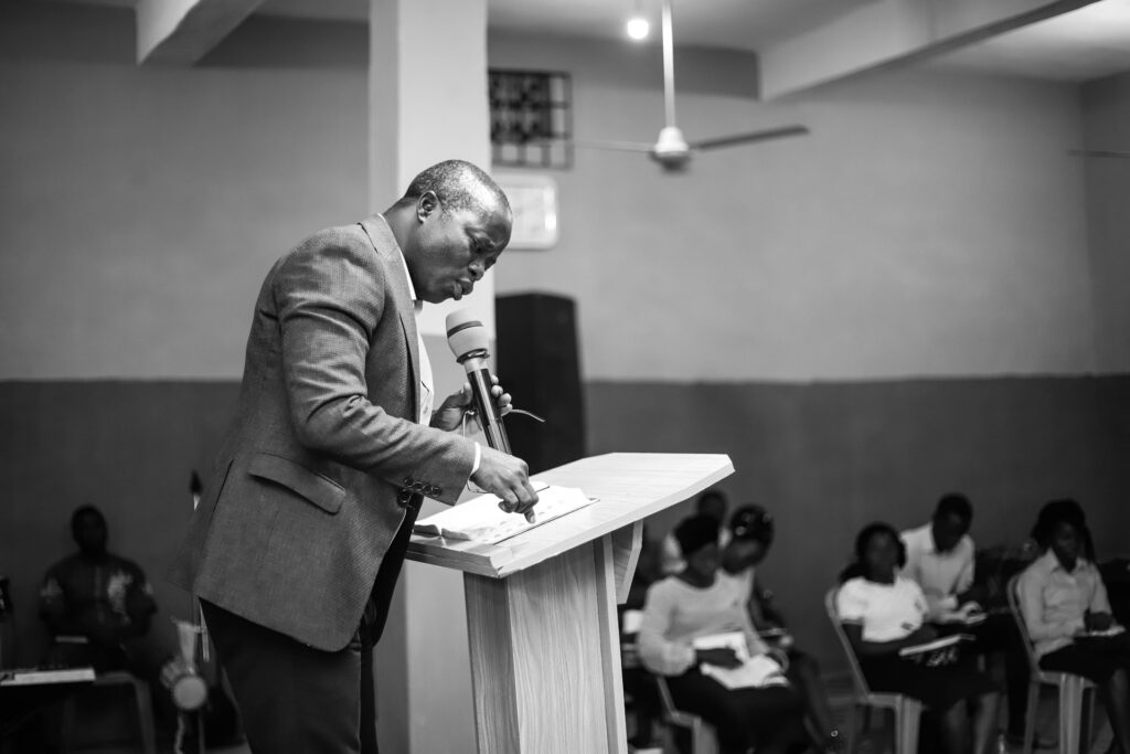 A Black pastor holds a microphone and preaches at a pulpit.