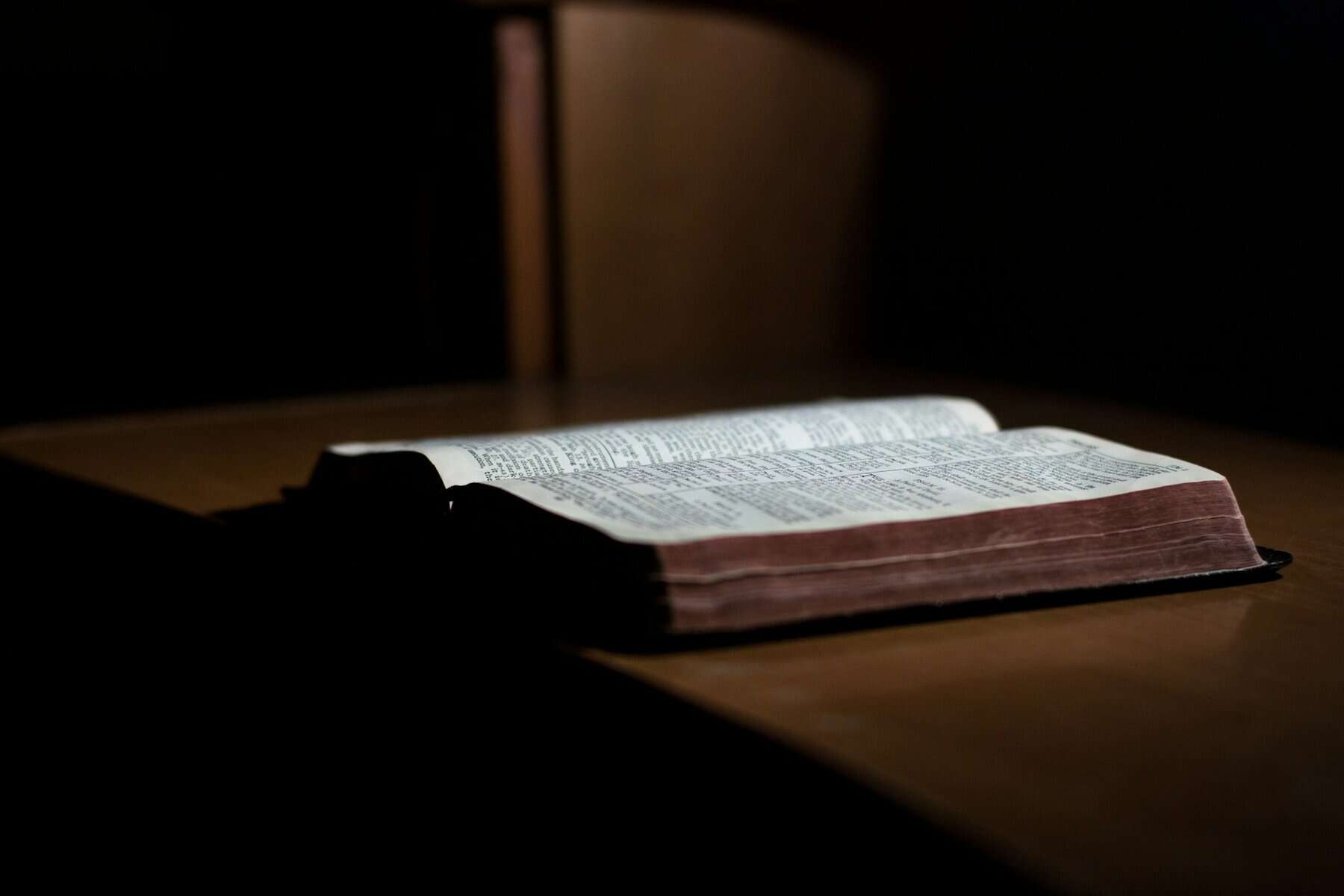 An open Bible on a desk in a dark setting.