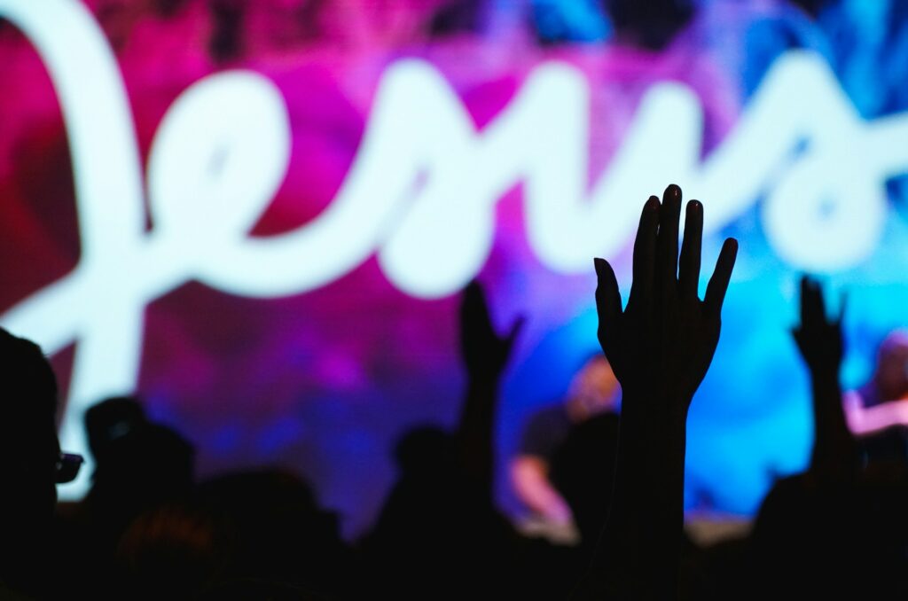 Silhouette of a hand in front of a Jesus neon sign.