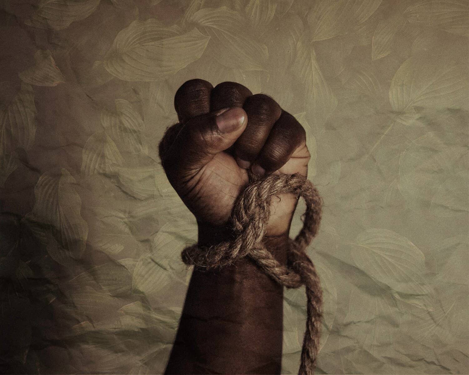 A Black man's raised fist with a loose rope around the wrist.