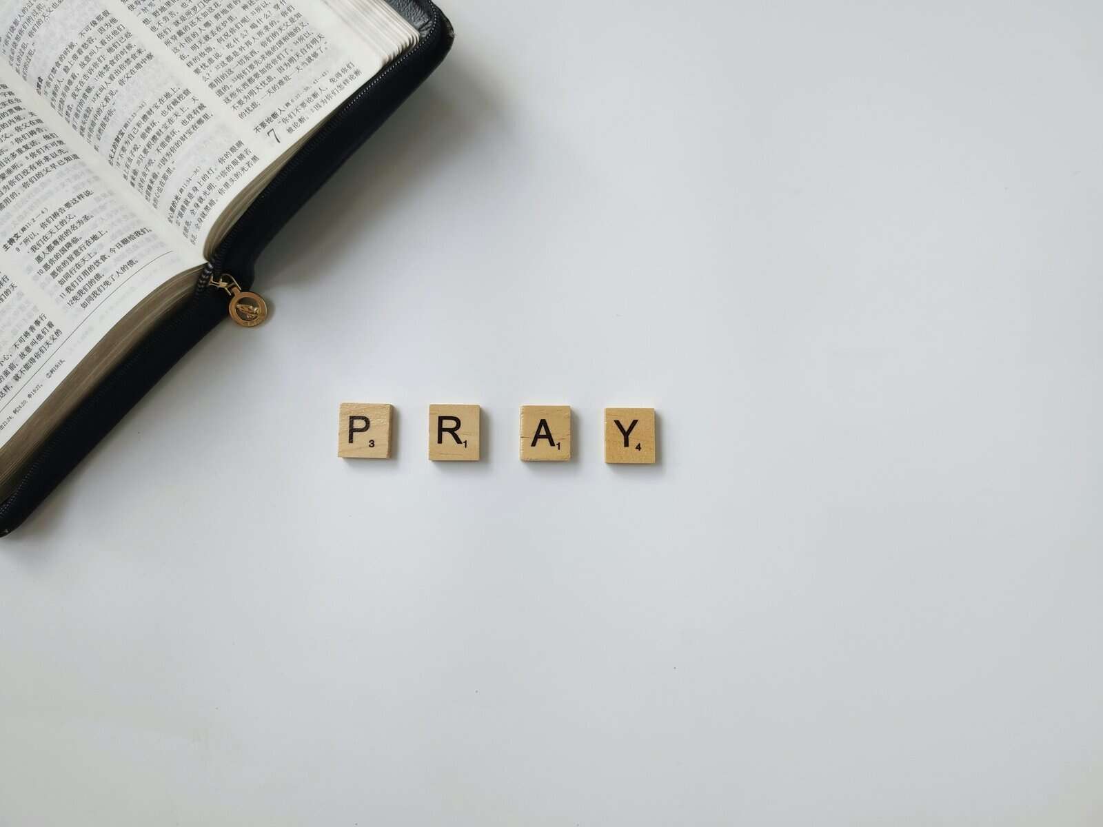 A portion of a Bible is shown with Scrabble tiles spelling PRAY.