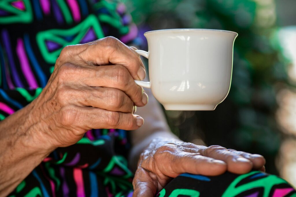 An elderly woman's hand holds a coffee cup.