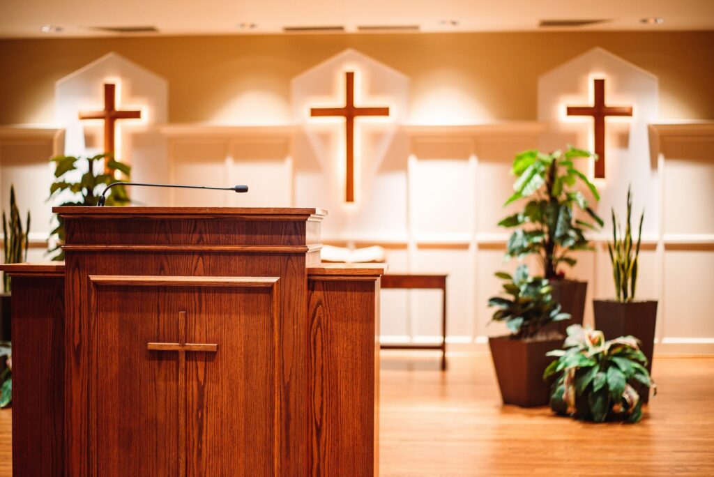 A wooden church pulpit with three lit crosses hung behind it.