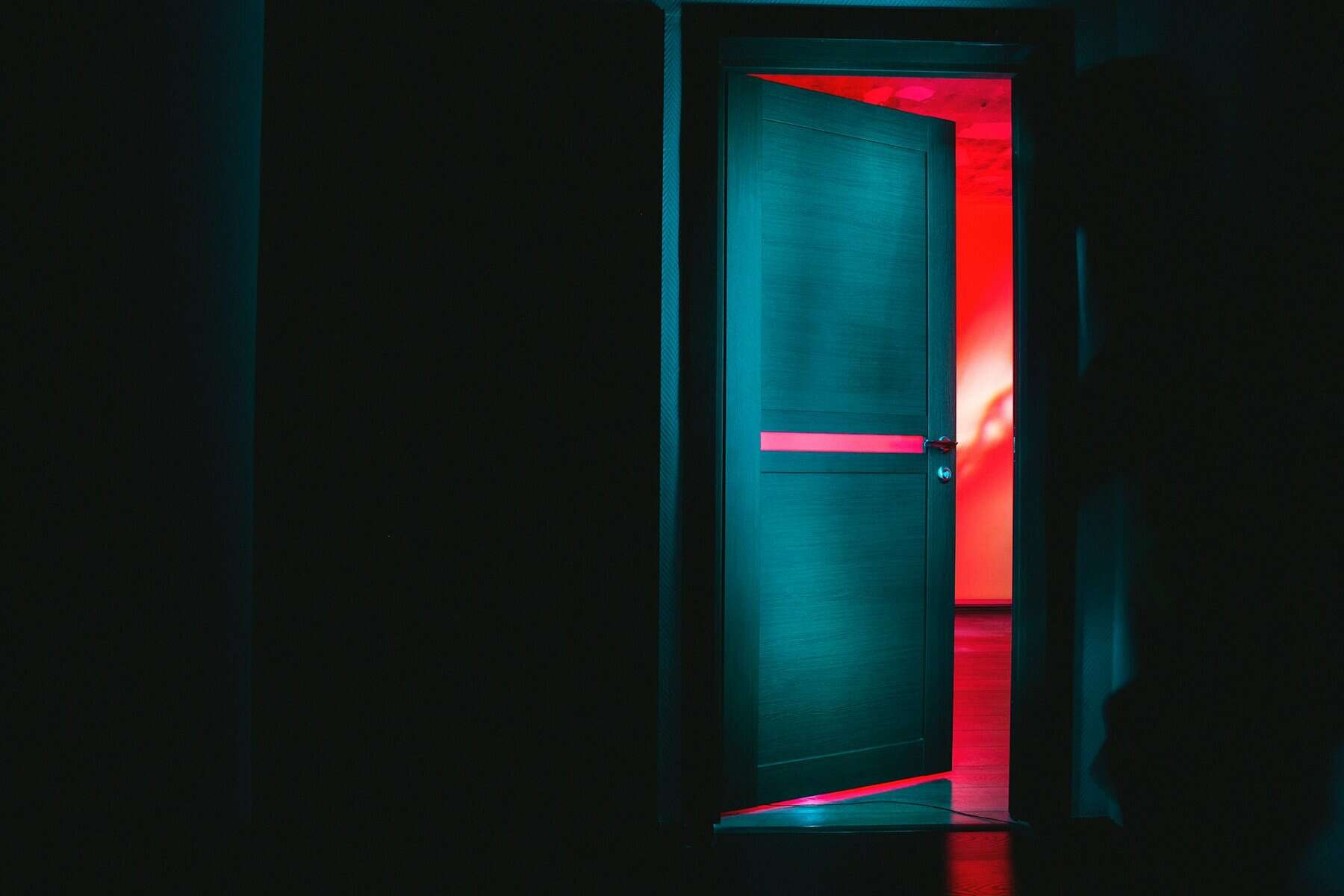 A green door opening into a red lit room.