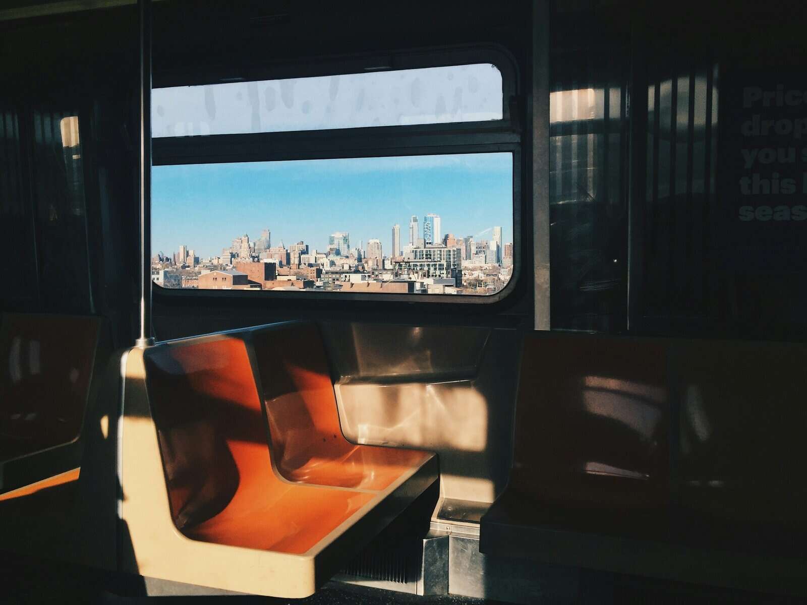 An NYC subway car seat with a skyline view out the window.