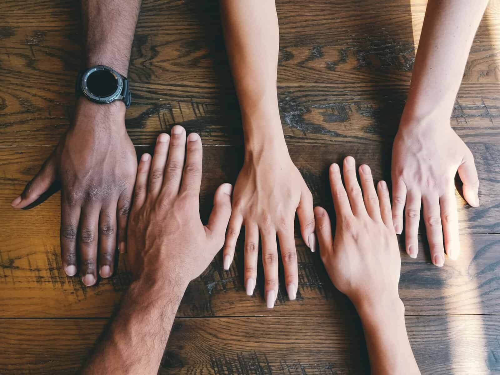 Hands of varying skin tones on a table.