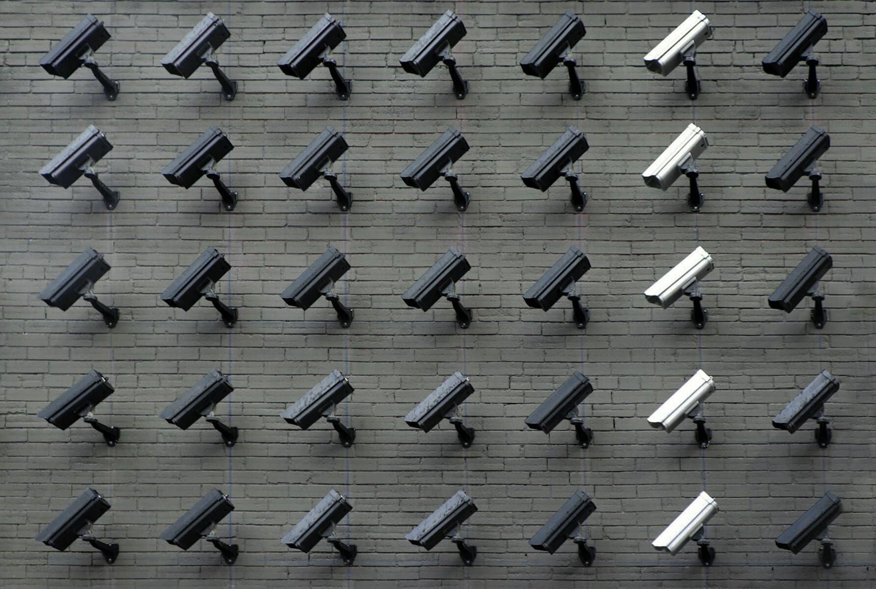 Rows of surveillance cameras on a brick wall.