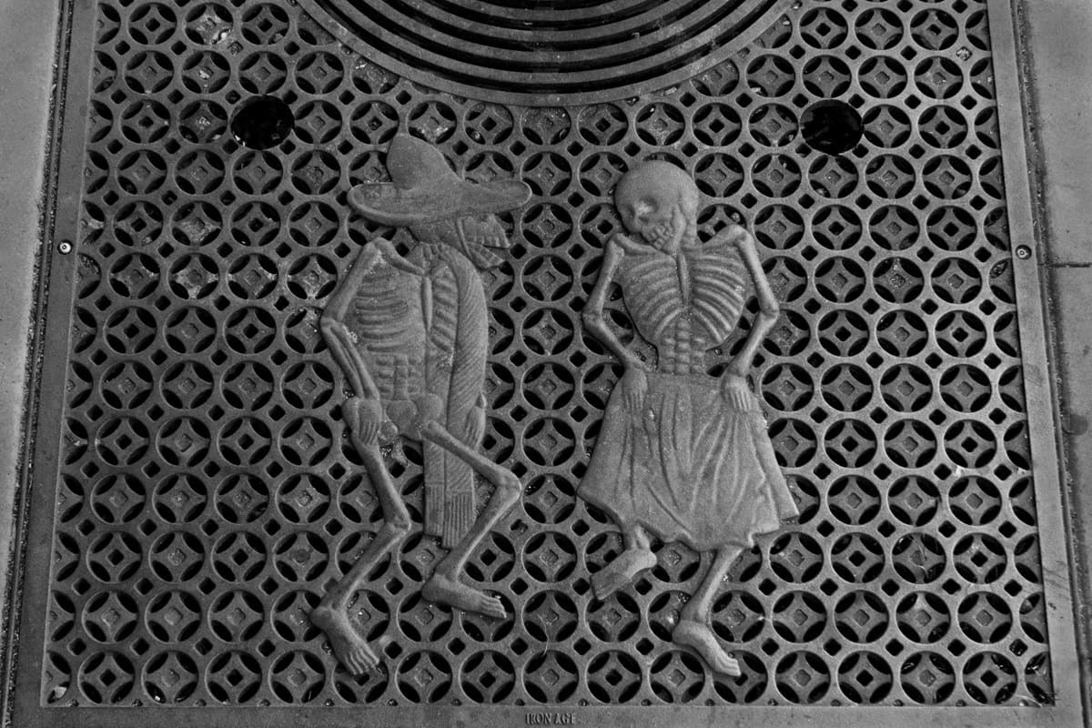 Two skeletons dancing on an iron street grate in San Francisco's Mission District.