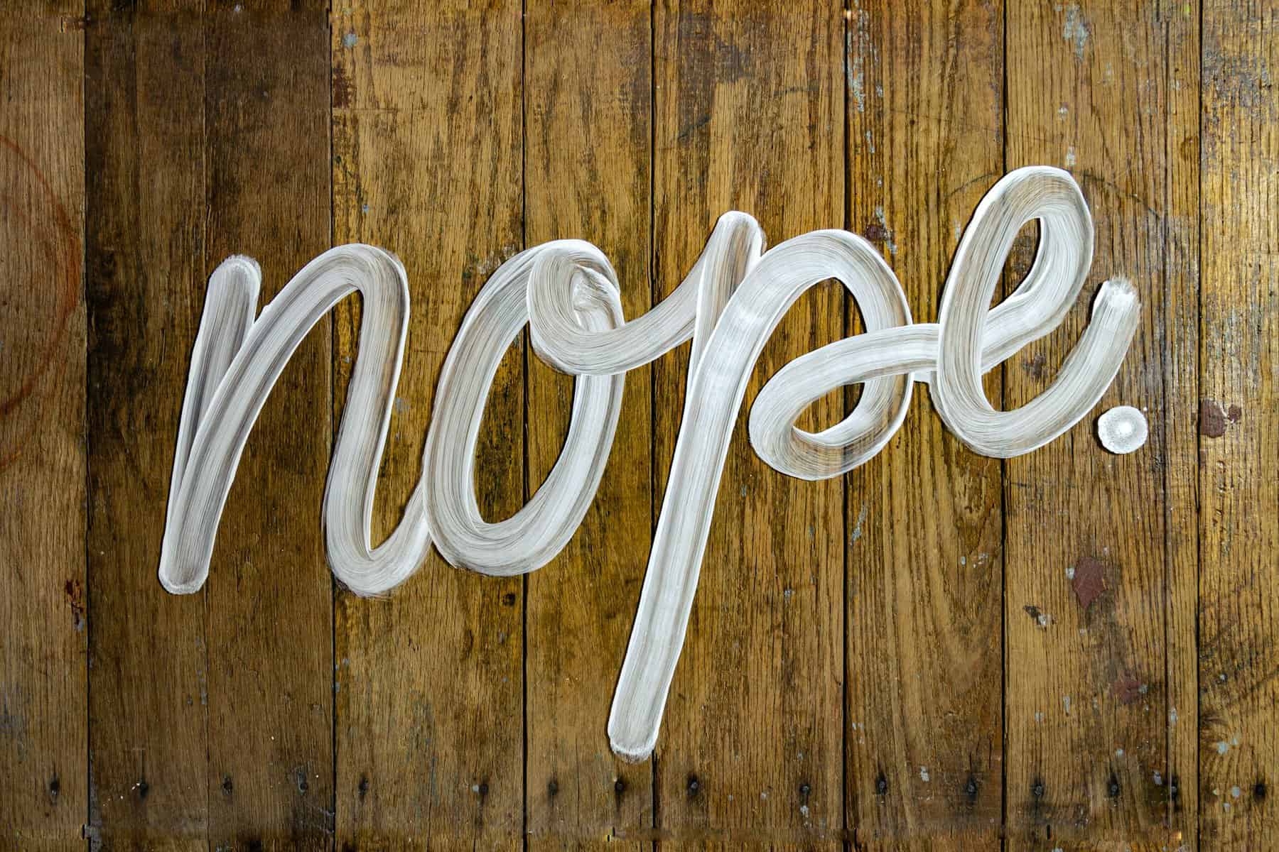 Nope written with a white substance on a wooden floor.