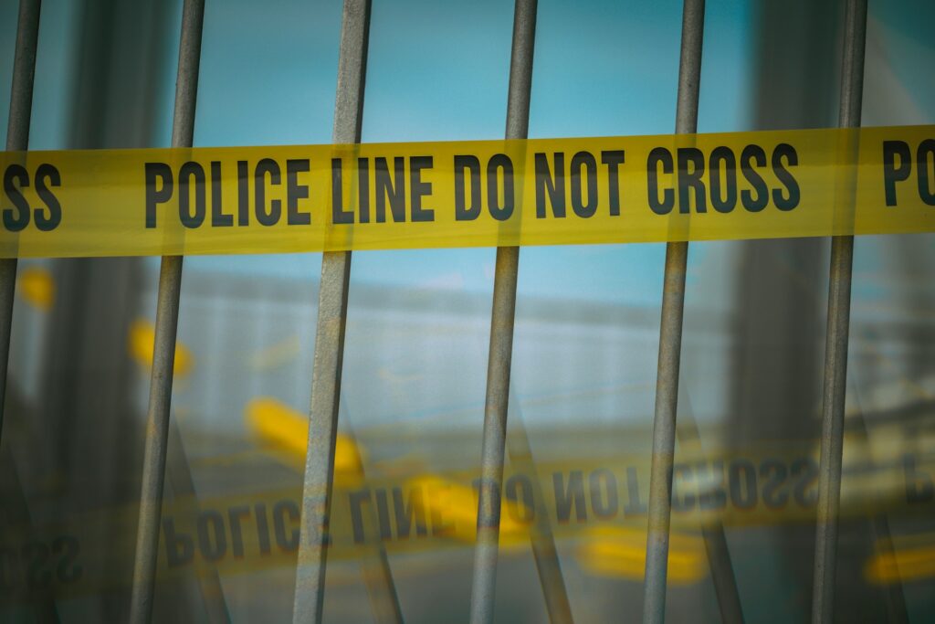A close-up of yellow police caution tape with black lettering, stretched across metal bars