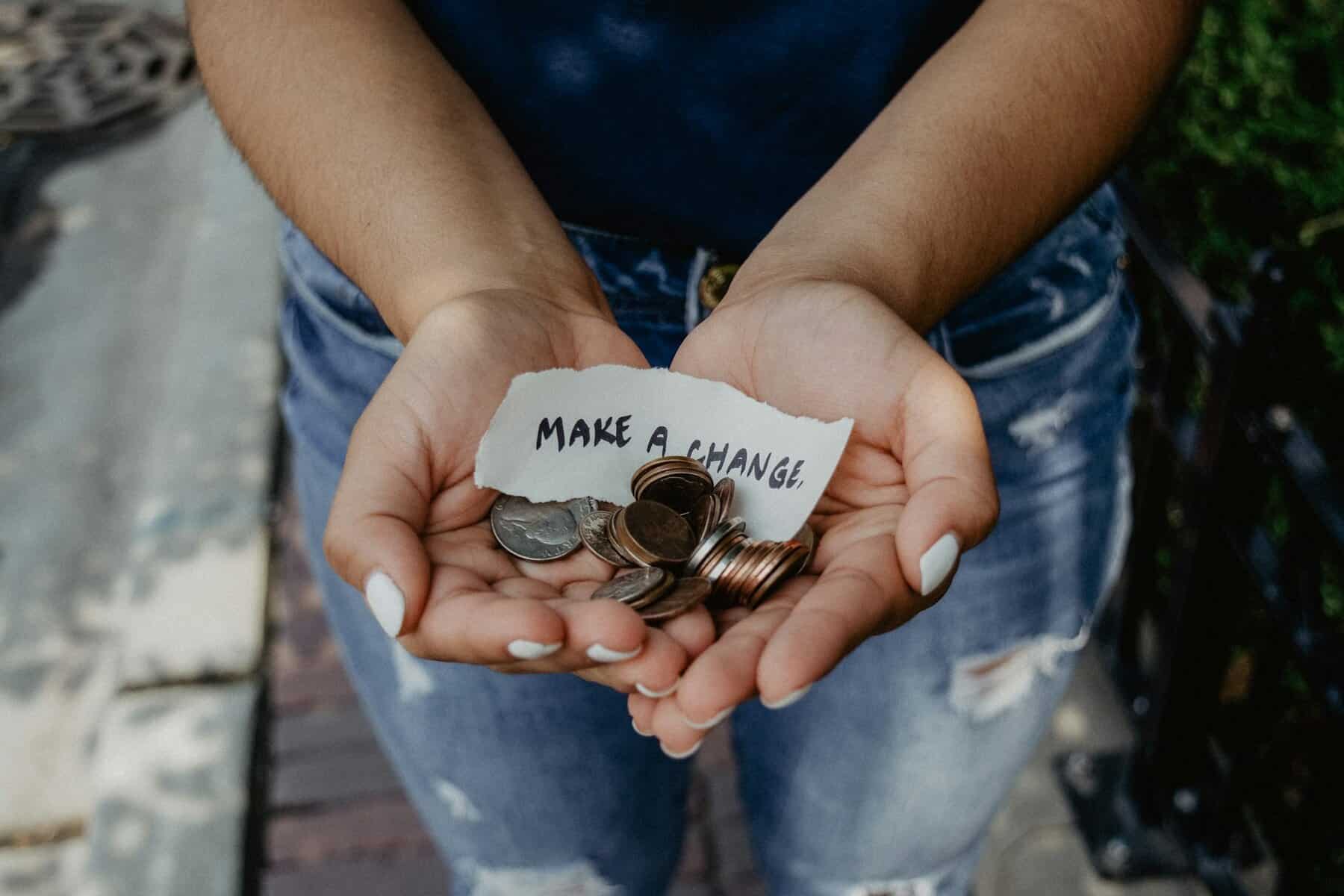 A person holding a handful of coins with a handwritten note "Make a Change."