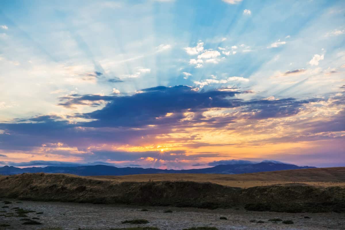 A sunset with clouds and God rays with mountains in the background and a dry creek bed in the foreground.