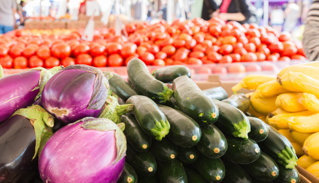 Colorful fresh vegetables including eggplants, zucchinis, and yellow squash at a farmers market.
