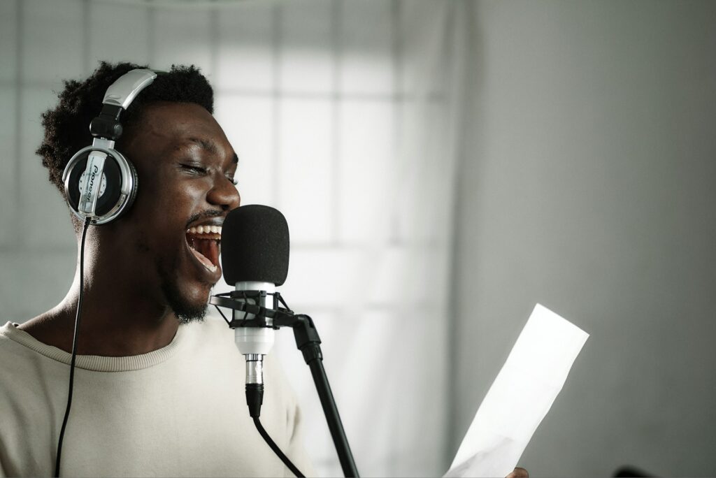 African male artist in front of a microphone with a headset on.