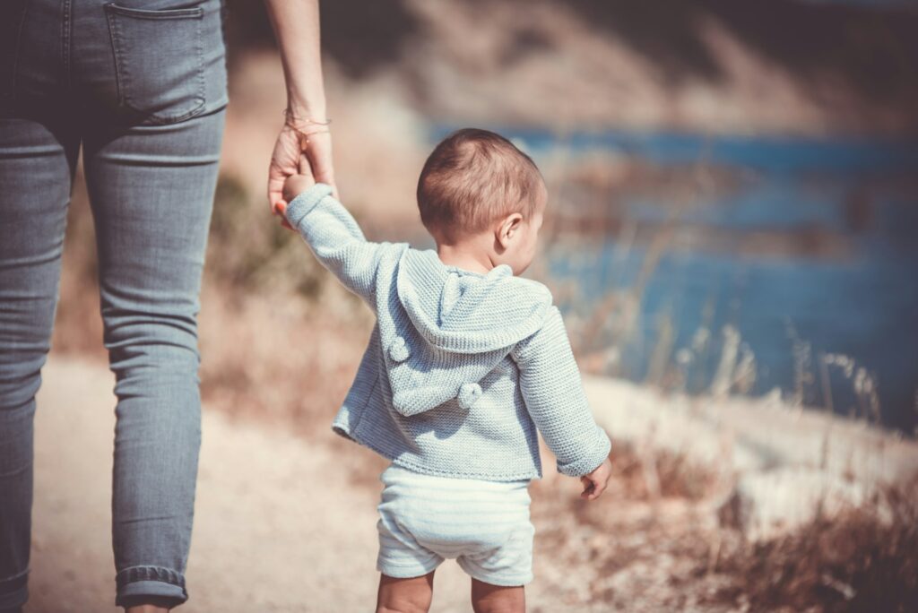 A woman holding a toddler's hand by a lake.