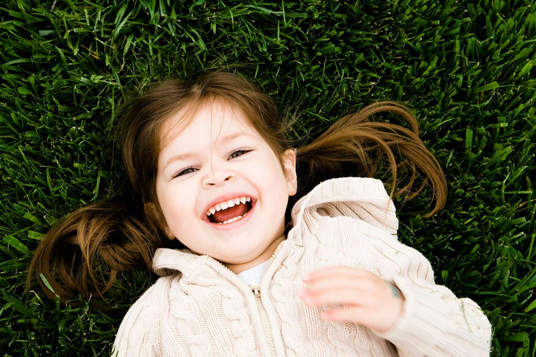 A smiling young girl lying on her back on grass.
