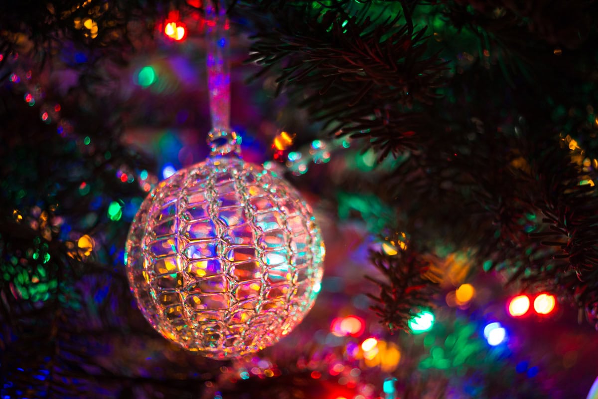The Holiday Season: The Story That Still Speaks A spun glass Christmas ornament hanging on a Christmas tree lit with colored lights.