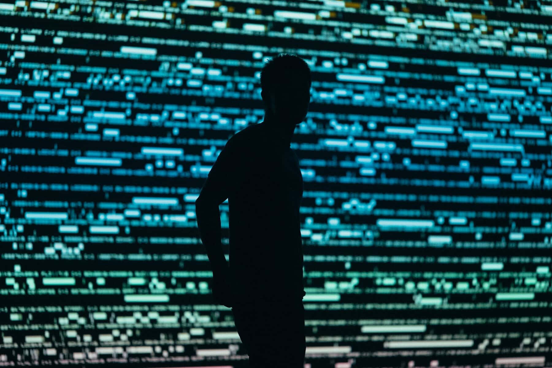 A young man in silhouette in front of a digital wall.