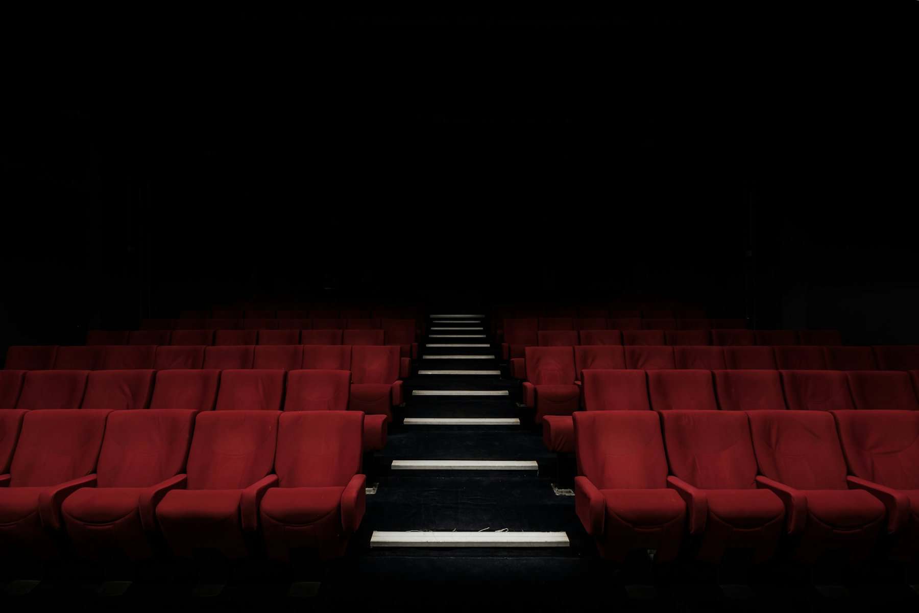 Rows of red movie theatre seats in low light.