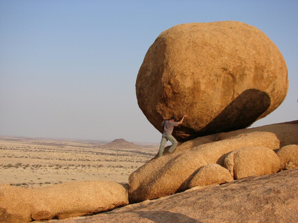A man with his hands on a massive boulder as if trying to move it.