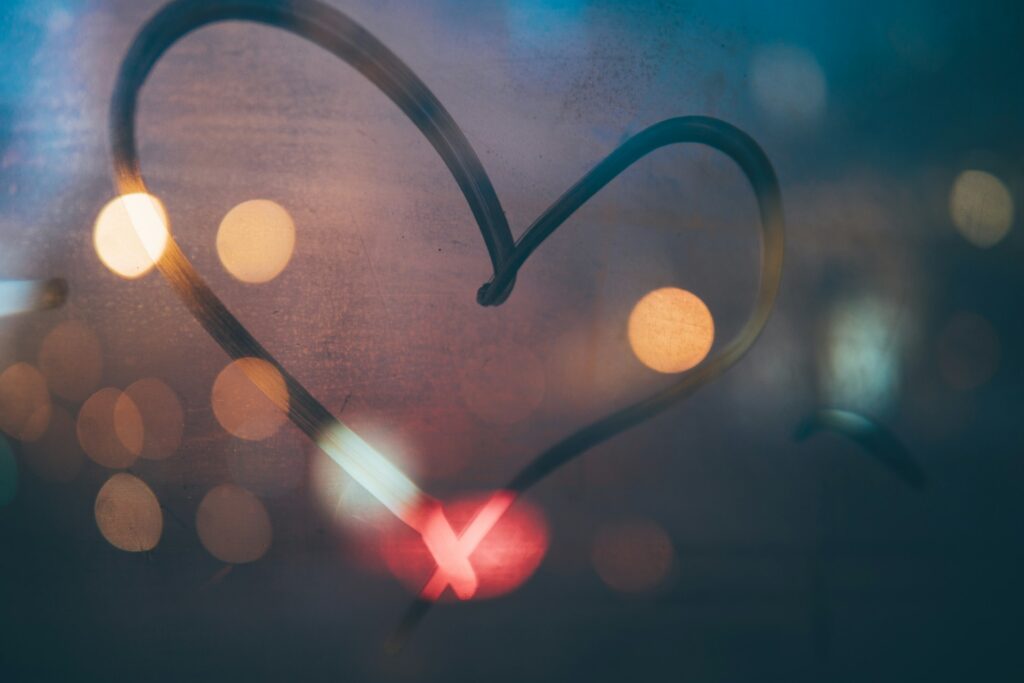 A heart drawn in vapor on a dark window with lights behind it