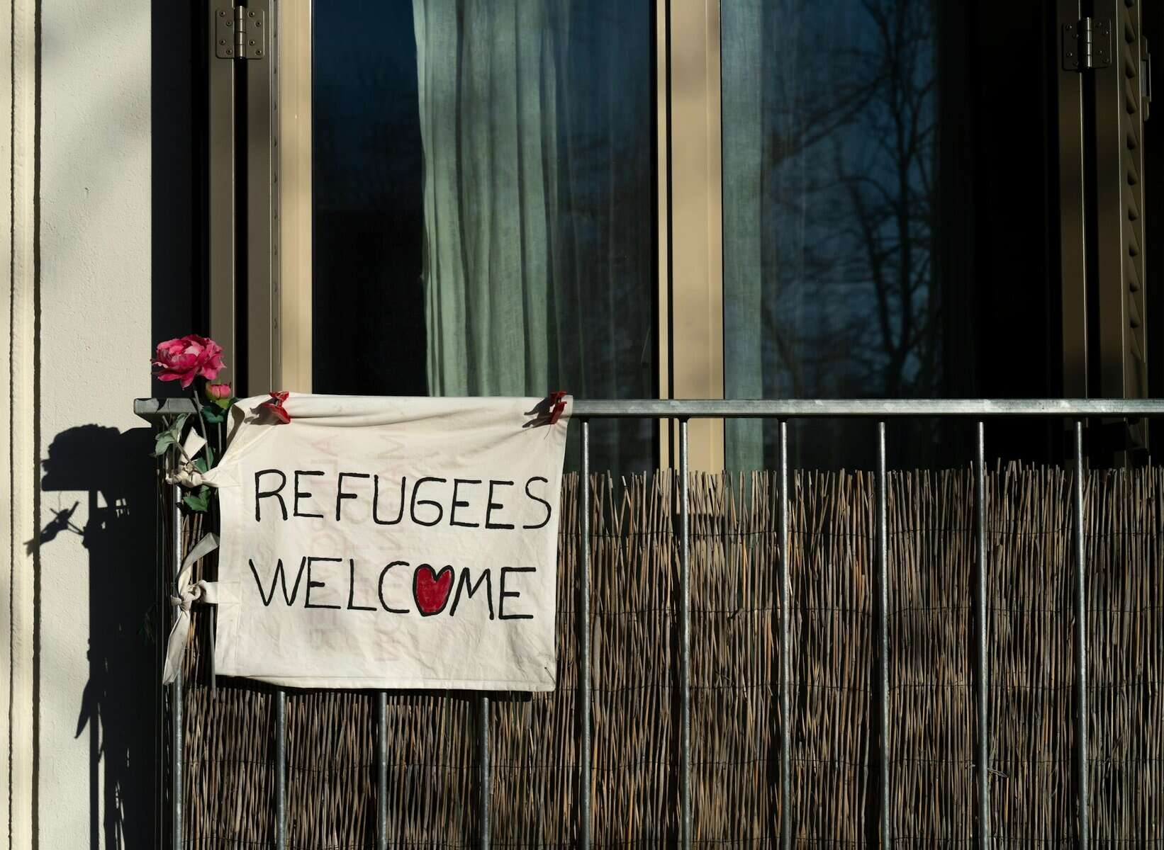 A handwritten sign affixed to a railing declares refugees welcome.